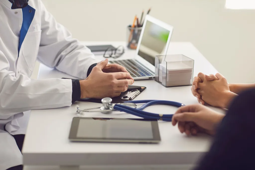 Confident Doctor and Couple Patient Sitting at the Table in Clinic Office. Family Doctor. - Dr. Ricardo Quadros - Neurocirurgião em BH